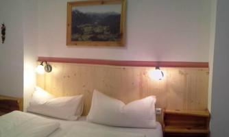 A cozy bedroom with two beds and wooden decor. A landscape picture hangs on the wall and there are bedside lamps.