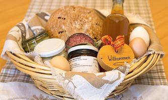 A basket with fresh groceries, including bread, eggs, various jars, and a bottle. A wooden sign with the inscription "Welcome" complements the arrangement.