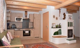A cozy kitchen with a modern design and rustic wooden ceilings. The room features a fireplace and a seating area with cushions.