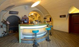A cozy bar with a curved counter and blue stools. The walls have a rustic style, and the lighting is warm and inviting.