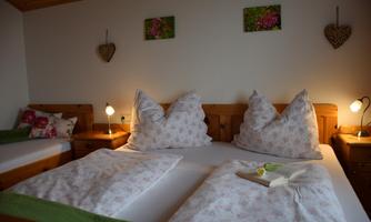 A cozy bedroom with a double bed and two pillows. Decorative pictures hang on the walls, and there is pleasant light from the bedside lamps.