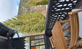 A cozy balcony with wooden furniture and a beautiful view of the surrounding nature. Tall trees and a clear sky create a relaxed atmosphere.