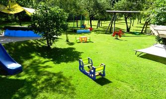 A beautiful garden with green lawn, playground equipment, and a splash pool. Trees provide shade and create an inviting atmosphere.