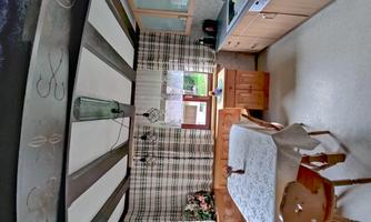 A bright kitchen with wooden cabinets, a white table, and a window with checkered curtains. The room is designed to be cozy and inviting.