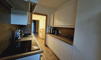 A modern kitchen with white cabinets and wooden surfaces. A further room is visible in the background.