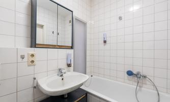 A modern bathroom with a bathtub, a sink, and a large mirror. The walls are tiled with white tiles.