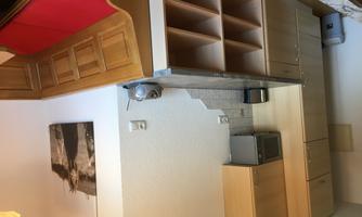 A modern kitchen with wooden cabinets and a counter. On the right, there is a bench with red cushions.