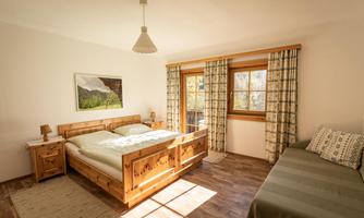 A cozy bedroom with a large wooden double bed and a single bed. Bright walls and large windows ensure plenty of daylight.