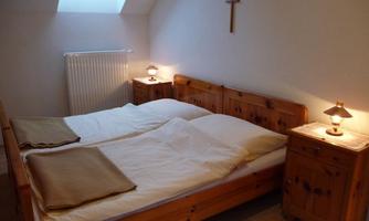 A cozy bedroom with a double bed and wooden furniture. The light from the bedside lamps creates a warm atmosphere.