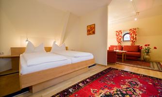 A bright room with two single beds and a cozy seating area. The carpet and the curtains give the room a warm atmosphere.