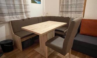 A cozy dining area with a wooden table and a corner bench. The walls are bright, and a small picture is attached to the wall.
