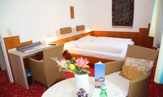A cozy room with a double bed and a small desk. In the foreground, there is a table with a flower vase and drinks.