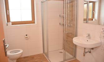 A modern bathroom with a shower cabin, a sink, and a toilet. The room has bright walls and a large window that lets in natural light.