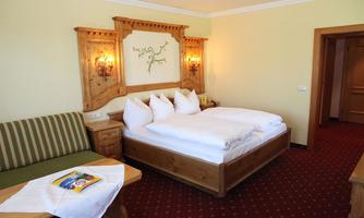 A cozy hotel room with a double bed and white pillows. A seating area and wooden decorations create an inviting atmosphere.
