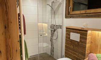 A modern bathroom with a shower, a toilet, and a wooden washbasin. The decor is bright and inviting, with towels in soft colors.