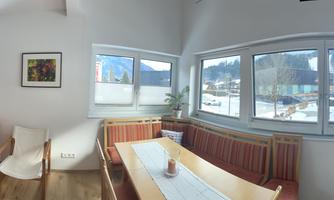 A bright living room with a red sofa and large windows overlooking a winter landscape. The room is modern and minimally furnished.