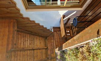 A balcony with wooden cladding and a small table-chair combination. In the background, a window with a golden frame can be seen.