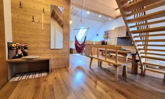 A modern room interior with wood paneling and bright colors. There is a staircase, a dining area, and a cozy hammock.