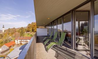 A modern terrace with loungers and a view of a picturesque landscape. In the background, trees and a church tower are visible.