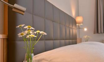 A modern bedroom with an upholstered headboard and a cozy duvet. On the bedside table, there is a vase with fresh flowers.