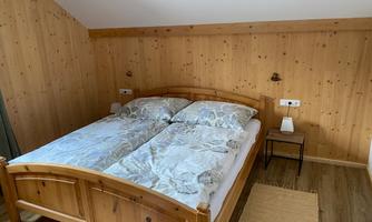 A cozy bedroom with a wooden bed and two mattresses. The walls are made of wood and there is a small bedside table next to the bed.