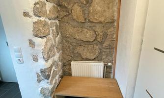 A cozy entrance area with a stone wall and a wooden bench. On the right is a modern door and a carpet lies on the floor.
