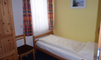 A simple room with a single bed and colorful curtains. There is a desk chair and a wooden wardrobe.