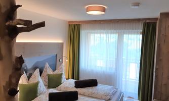 A cozy bedroom with two beds, pretty pillows, and bedspreads. Large windows let in plenty of light and offer a view outside.