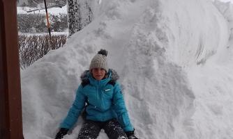 Two children are playing in the snow. One is sitting on a large snow mound, while the other is standing on top of it.