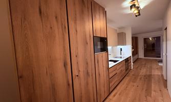 A modern kitchen with wooden cabinets and a bright countertop. The room is stylish and well-lit.