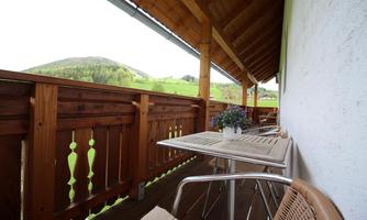 A beautiful balcony with a wooden railing and a table. In the background, there are green hills and trees.visible.