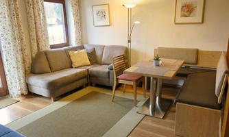 A cozy living room with a beige sofa, a dining table, and modern chairs. Large windows let in plenty of daylight, creating an inviting atmosphere.