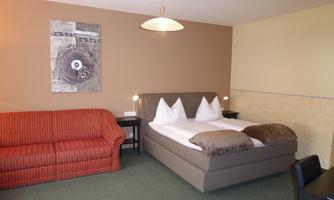 A cozy room with a double bed and a red sofa. The walls are painted in warm colors and there is a modern ceiling lamp.