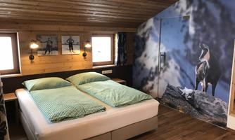 A cozy bedroom with a double bed and checkered bedspreads. The walls are made of wood and there is a beautiful mural of an animal.