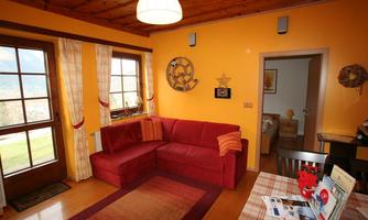 A cozy living room with a red sofa corner and orange-colored walls. Large windows let in a lot of light and offer a view outside.