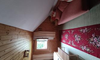 A cozy room with wood paneling and a sloped ceiling. There is a bed, a couch, and a carpet with a floral pattern.