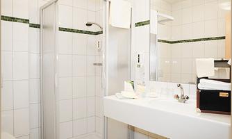A bright bathroom with a shower cubicle and a vanity. The wall tiles are white with green accents.
