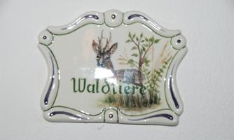 A ceramic plaque featuring an image of a deer and the inscription "Forest Animals." It has a curved shape and a decorative frame.