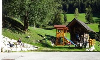 A beautiful garden with a playground and a small cabin. In the background, green meadows and trees can be seen.
