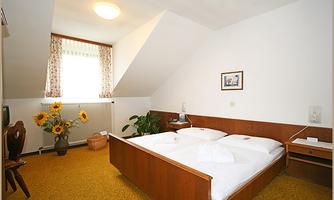 A cozy bedroom with a double bed and a large window. Sunflowers and a desk complement the decor.