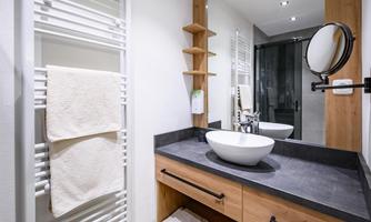 A modern bathroom with wood and stone accents. It features a sink, a large mirror, and towel holders.