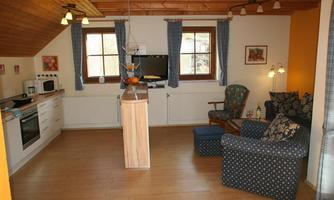 A cozy living kitchen with modern furniture and warm wooden elements. The room is bright and inviting, with large windows and a pleasant atmosphere.