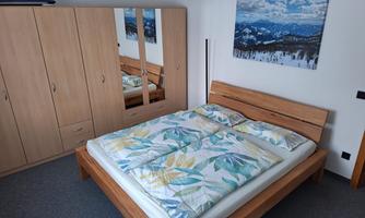 A modern bedroom with a large bed and a bright comforter. A picture of a mountain landscape hangs on the wall, and a wardrobe with mirrors is present.