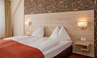 A cozy bedroom with a double bed and two pillows. The walls are decorated with a modern pattern and there is warm lighting.