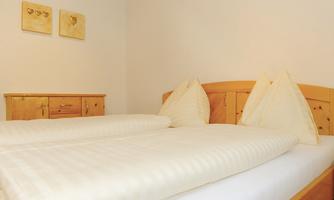 A cozy bedroom with two single beds and bright pillows. On the wall hang two pictures with heart motifs.