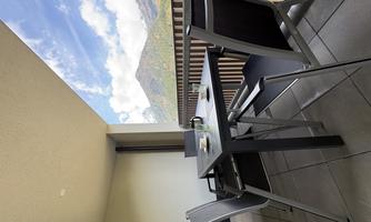 A modern furnished balcony with a table and chairs. In the background, mountains and a blue sky can be seen.