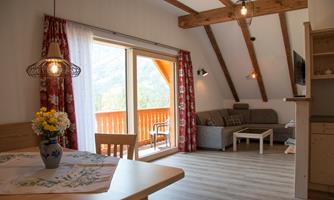 A cozy living room with wooden ceilings and spacious windows. There is a table with flowers and a comfortable couch that looks inviting.
