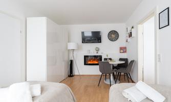 A modern room with two beds, a fluffy carpet, and a TV on the wall. A cozy seating area with an electric fireplace and a table for two completes the space.