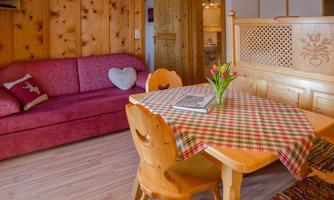 A cozy living space with a red sofa and a wooden dining table. Fresh tulips and a book are on the table.