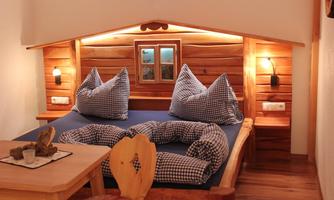 A cozy bedroom with a wooden frame bed and large pillows. Soft lighting and a small table create a relaxed atmosphere.